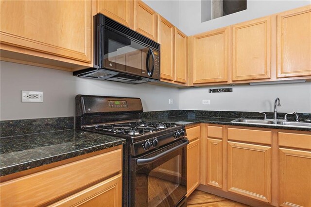 kitchen with dark stone countertops, sink, light hardwood / wood-style flooring, and black appliances