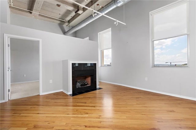 unfurnished living room with light hardwood / wood-style flooring, a tiled fireplace, and a towering ceiling