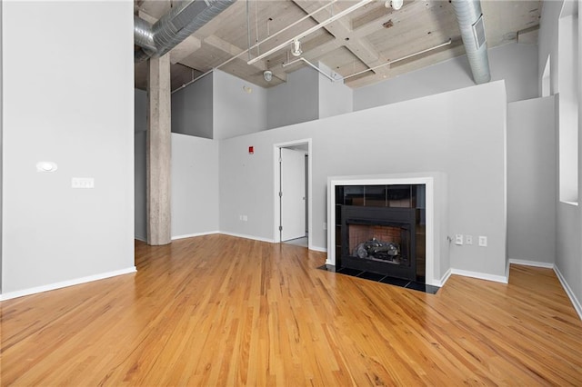 unfurnished living room with a fireplace, rail lighting, light wood-type flooring, and a high ceiling