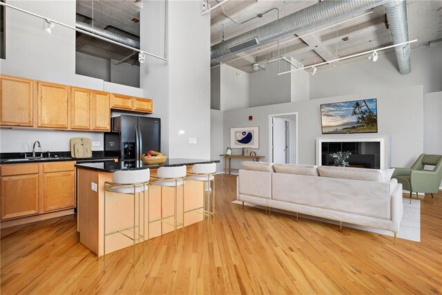 kitchen featuring a high ceiling, light wood-type flooring, black refrigerator with ice dispenser, a kitchen breakfast bar, and track lighting