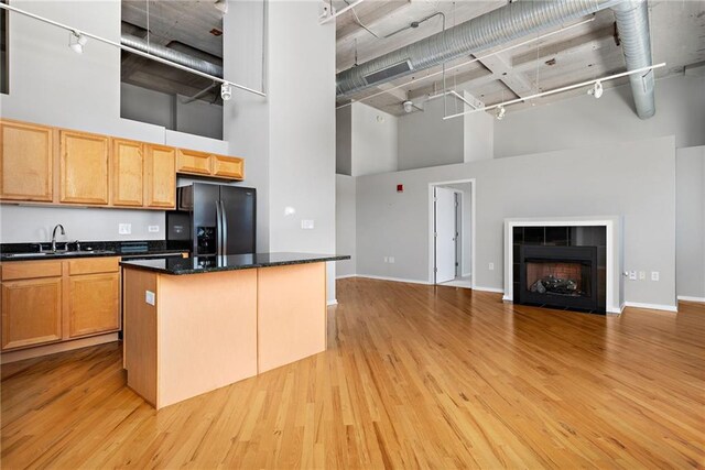 kitchen featuring black refrigerator with ice dispenser, a fireplace, light wood-type flooring, and a high ceiling