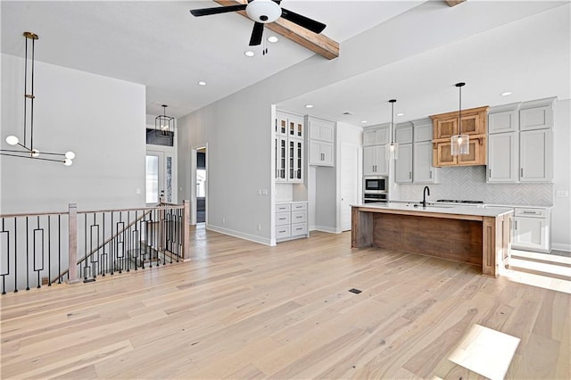 kitchen with sink, beam ceiling, pendant lighting, light hardwood / wood-style floors, and an island with sink