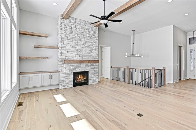 unfurnished living room featuring beamed ceiling, light hardwood / wood-style flooring, a stone fireplace, and plenty of natural light