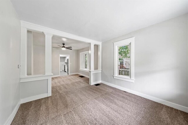 spare room with decorative columns, light carpet, and ceiling fan