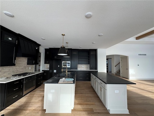 kitchen with appliances with stainless steel finishes, dark countertops, a kitchen island with sink, and dark cabinets