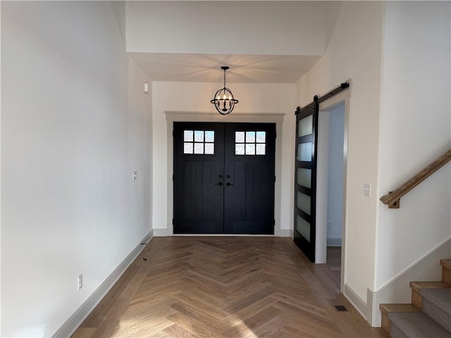 entrance foyer featuring a barn door, a notable chandelier, visible vents, baseboards, and stairway