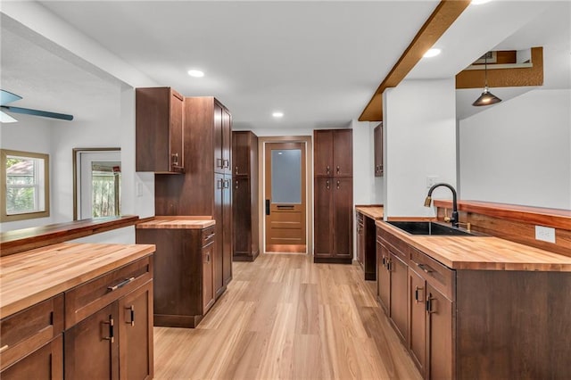 kitchen with light hardwood / wood-style flooring, butcher block counters, ceiling fan, hanging light fixtures, and sink