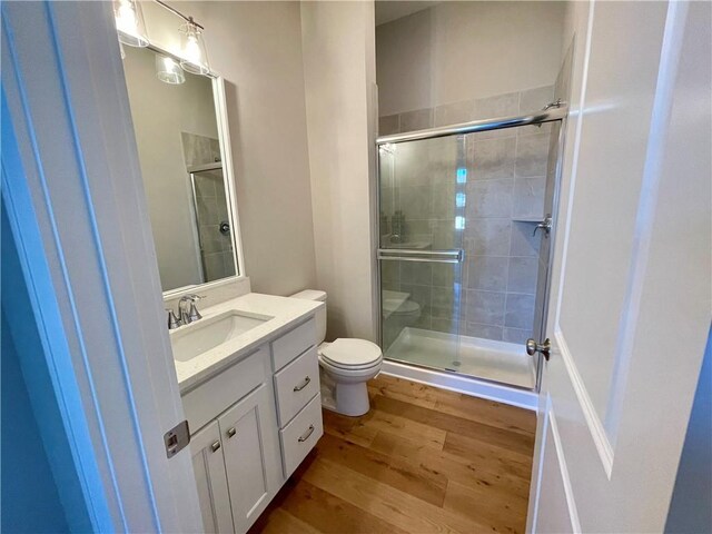 bathroom with hardwood / wood-style flooring, vanity, toilet, and a shower with shower door