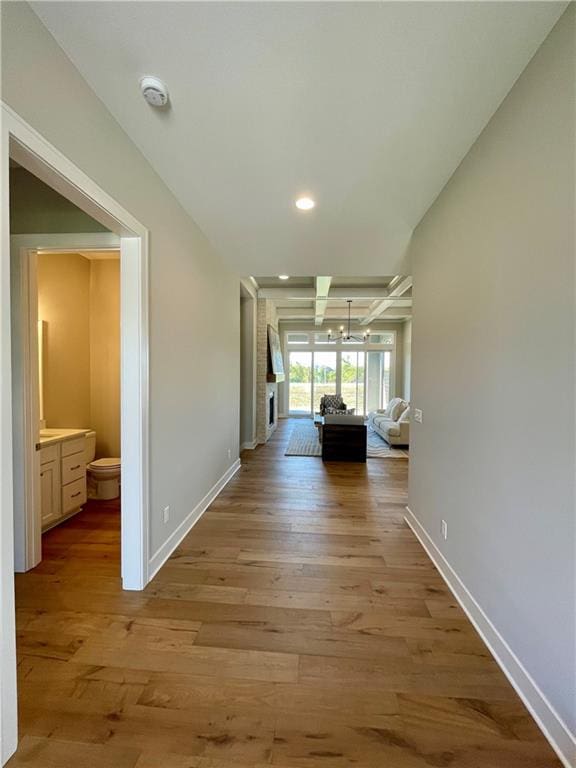 hallway featuring beamed ceiling, a chandelier, and light wood-type flooring