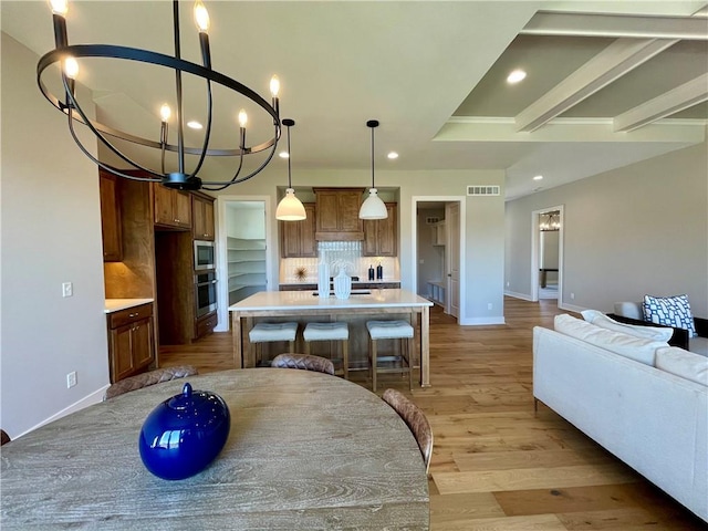 kitchen featuring appliances with stainless steel finishes, pendant lighting, tasteful backsplash, an island with sink, and light hardwood / wood-style flooring