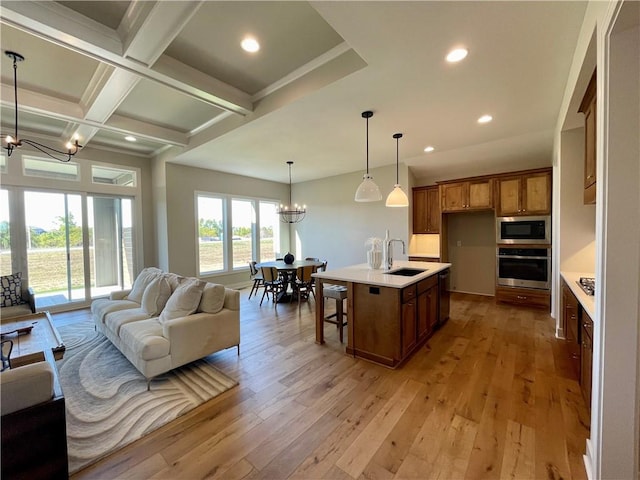 kitchen featuring oven, coffered ceiling, a kitchen island with sink, a notable chandelier, and beam ceiling