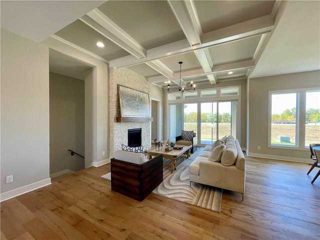 living room with coffered ceiling, a stone fireplace, light hardwood / wood-style flooring, a notable chandelier, and beam ceiling