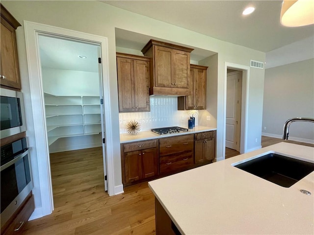 kitchen with sink, backsplash, light hardwood / wood-style floors, and appliances with stainless steel finishes