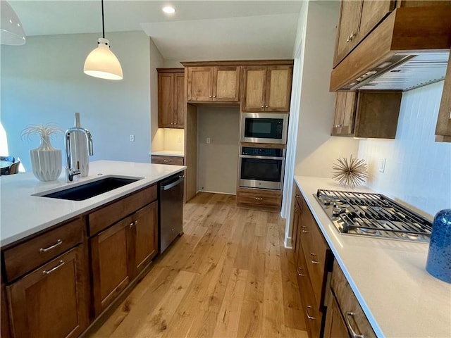 kitchen with premium range hood, sink, light wood-type flooring, pendant lighting, and stainless steel appliances