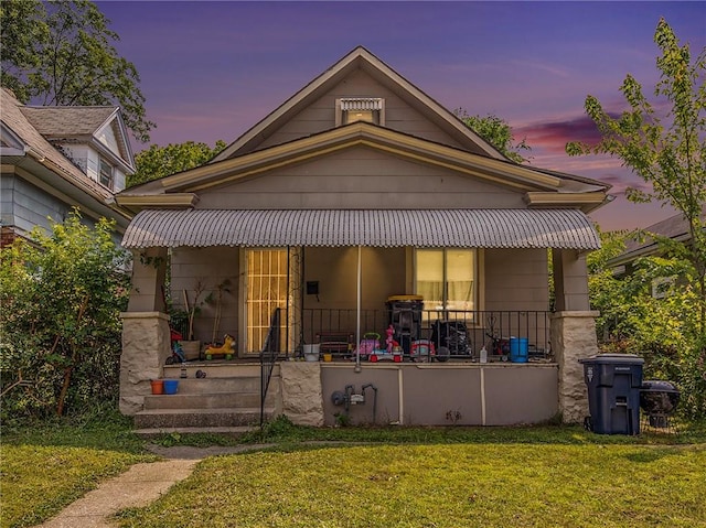 back house at dusk featuring covered porch and a lawn