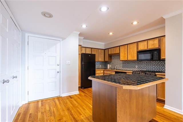 kitchen featuring tile countertops, backsplash, brown cabinetry, light wood-style floors, and black appliances