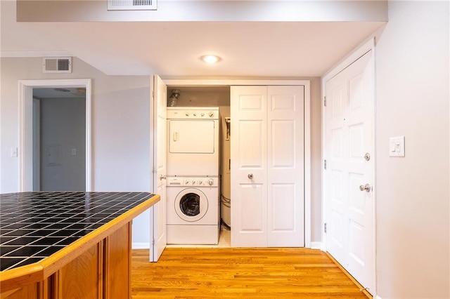 laundry area featuring light wood-style floors, stacked washer / drying machine, laundry area, and visible vents