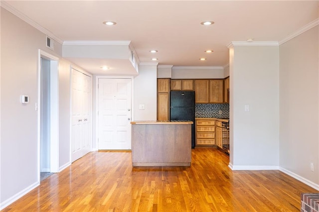 kitchen featuring brown cabinets, light wood finished floors, backsplash, ornamental molding, and freestanding refrigerator