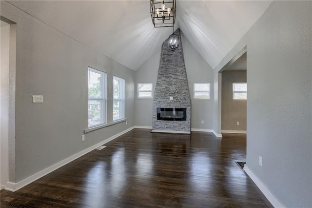 unfurnished living room with vaulted ceiling, a stone fireplace, dark wood-type flooring, and an inviting chandelier