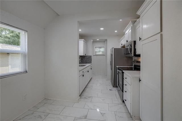 kitchen with tasteful backsplash, lofted ceiling, sink, white cabinets, and stainless steel appliances