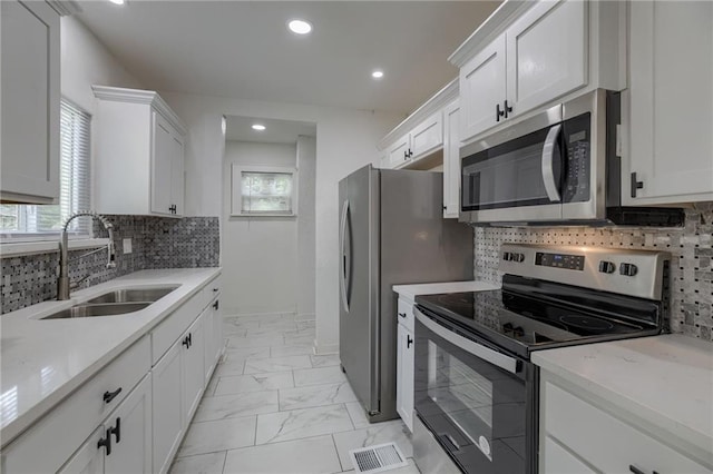 kitchen featuring appliances with stainless steel finishes, sink, white cabinets, backsplash, and light stone counters