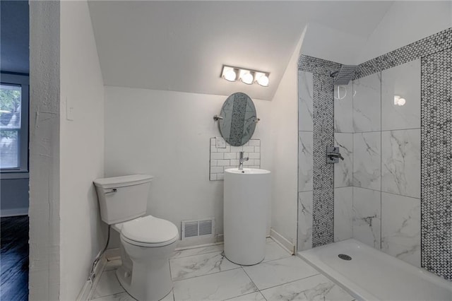 bathroom featuring vaulted ceiling, a tile shower, and toilet