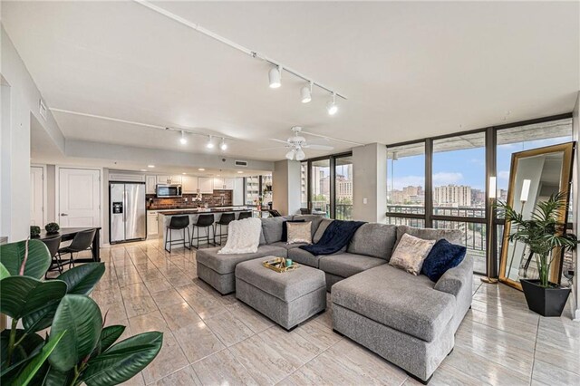 tiled living room with ceiling fan, a wall of windows, and track lighting