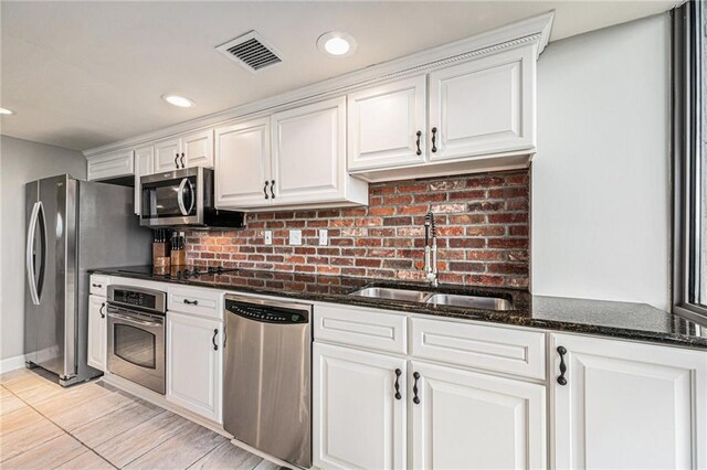 kitchen with decorative backsplash, dark stone counters, white cabinets, stainless steel appliances, and sink