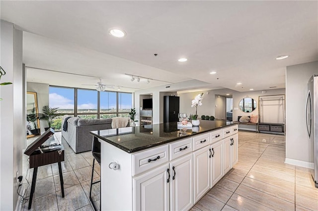 kitchen featuring a kitchen island, stainless steel refrigerator, dark stone countertops, white cabinets, and a kitchen breakfast bar