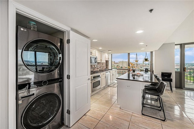 kitchen with white cabinetry, backsplash, stacked washer / dryer, appliances with stainless steel finishes, and a breakfast bar area