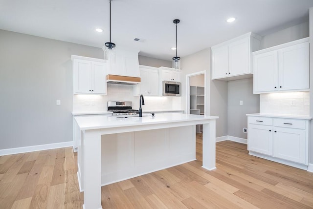 kitchen featuring white cabinetry, hanging light fixtures, stainless steel appliances, a center island with sink, and light wood-type flooring