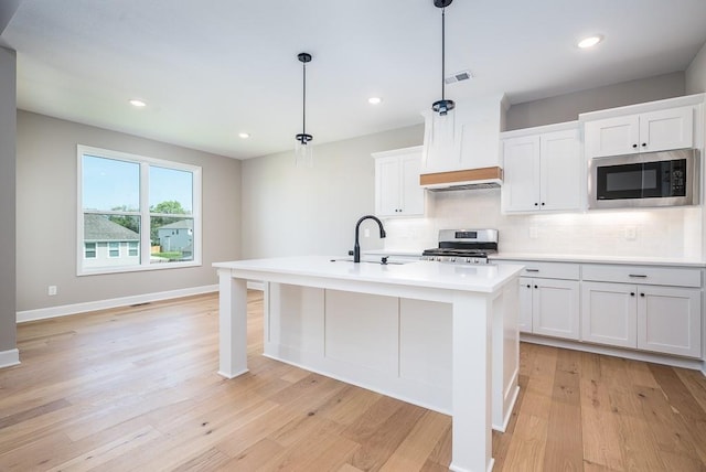 kitchen featuring built in microwave, white cabinetry, hanging light fixtures, a center island with sink, and stainless steel range