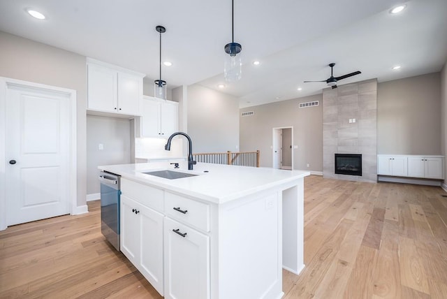 kitchen featuring sink, white cabinetry, stainless steel dishwasher, pendant lighting, and a kitchen island with sink