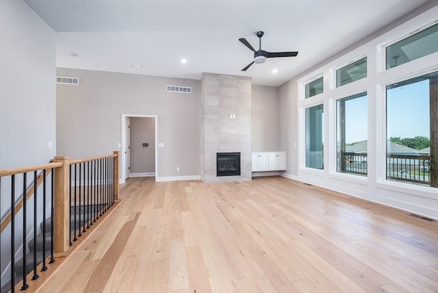 unfurnished living room featuring a tile fireplace, light hardwood / wood-style floors, and ceiling fan