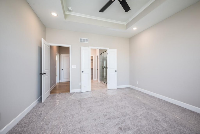 unfurnished bedroom with light carpet, ceiling fan, and a tray ceiling