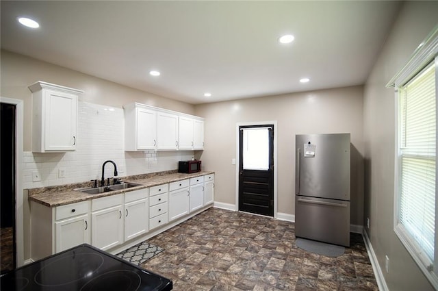 kitchen with stainless steel refrigerator, tasteful backsplash, sink, white cabinets, and dark stone counters