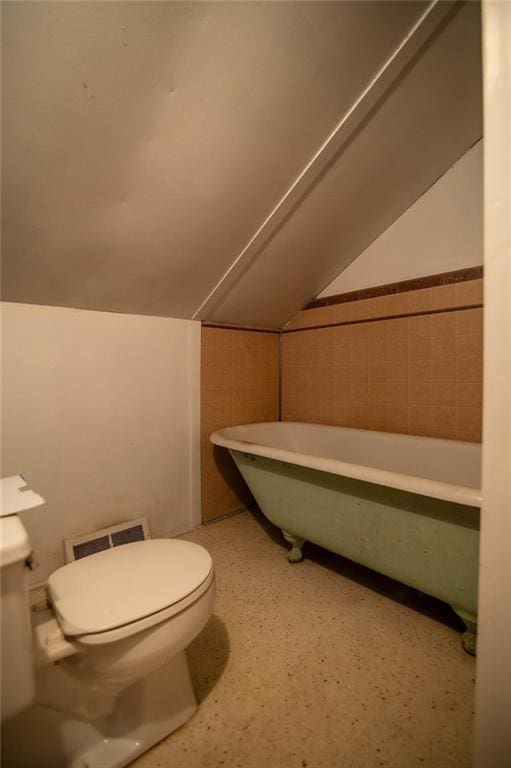 bathroom with a bathtub, vaulted ceiling, and toilet