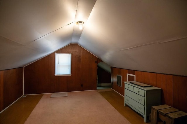 additional living space featuring light colored carpet, vaulted ceiling, and wood walls