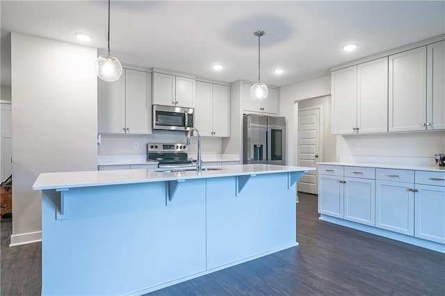 kitchen with hanging light fixtures, appliances with stainless steel finishes, and an island with sink