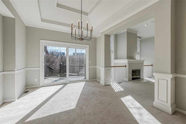 unfurnished dining area featuring crown molding, an inviting chandelier, light carpet, a tray ceiling, and a fireplace