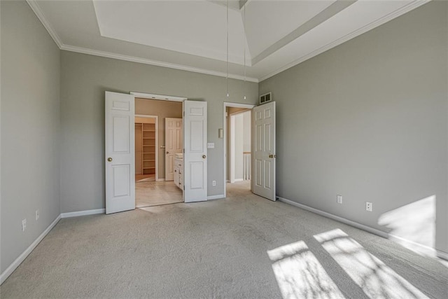 unfurnished bedroom with light colored carpet, ornamental molding, a tray ceiling, and a spacious closet