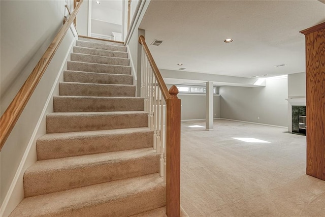 stairway featuring a high end fireplace and carpet floors