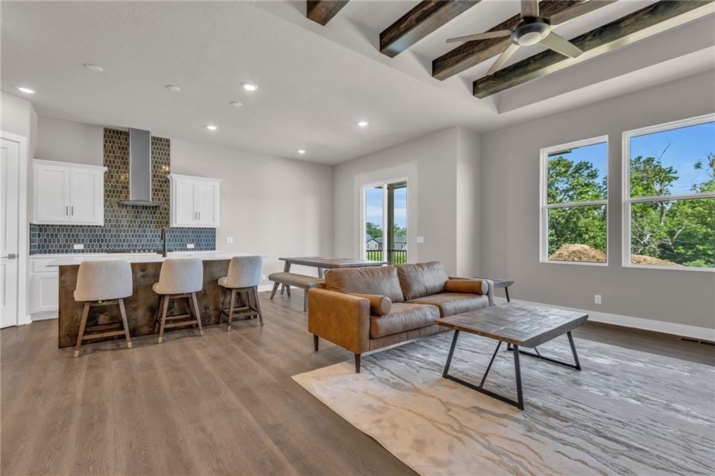 living room featuring beamed ceiling, light hardwood / wood-style floors, and ceiling fan