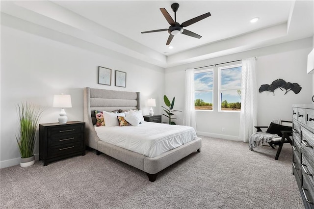 carpeted bedroom with a raised ceiling and ceiling fan