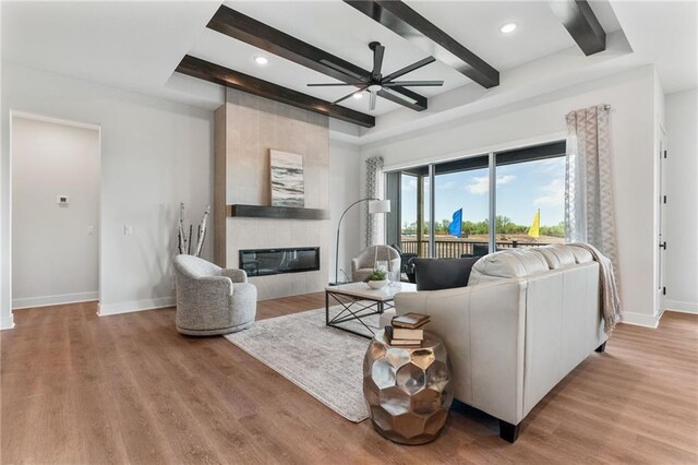 living room with ceiling fan, wood-type flooring, beam ceiling, and a large fireplace