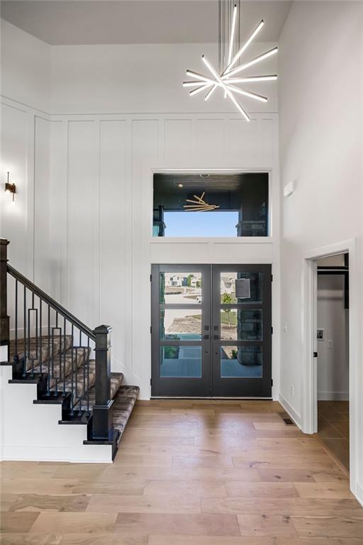 foyer with a high ceiling, an inviting chandelier, light hardwood / wood-style floors, and french doors