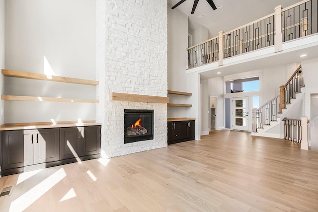 unfurnished living room featuring baseboards, a fireplace, ceiling fan, light wood-style floors, and a high ceiling