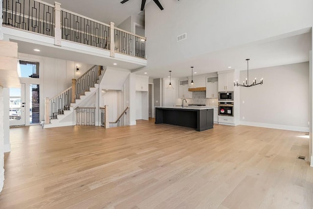 unfurnished living room featuring ceiling fan with notable chandelier, baseboards, a sink, visible vents, and light wood-style flooring