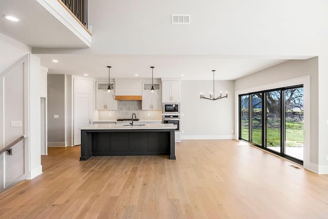 kitchen with light countertops, a sink, built in microwave, visible vents, and white cabinets
