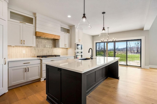 kitchen with light countertops, backsplash, a sink, stainless steel appliances, and light wood-style floors